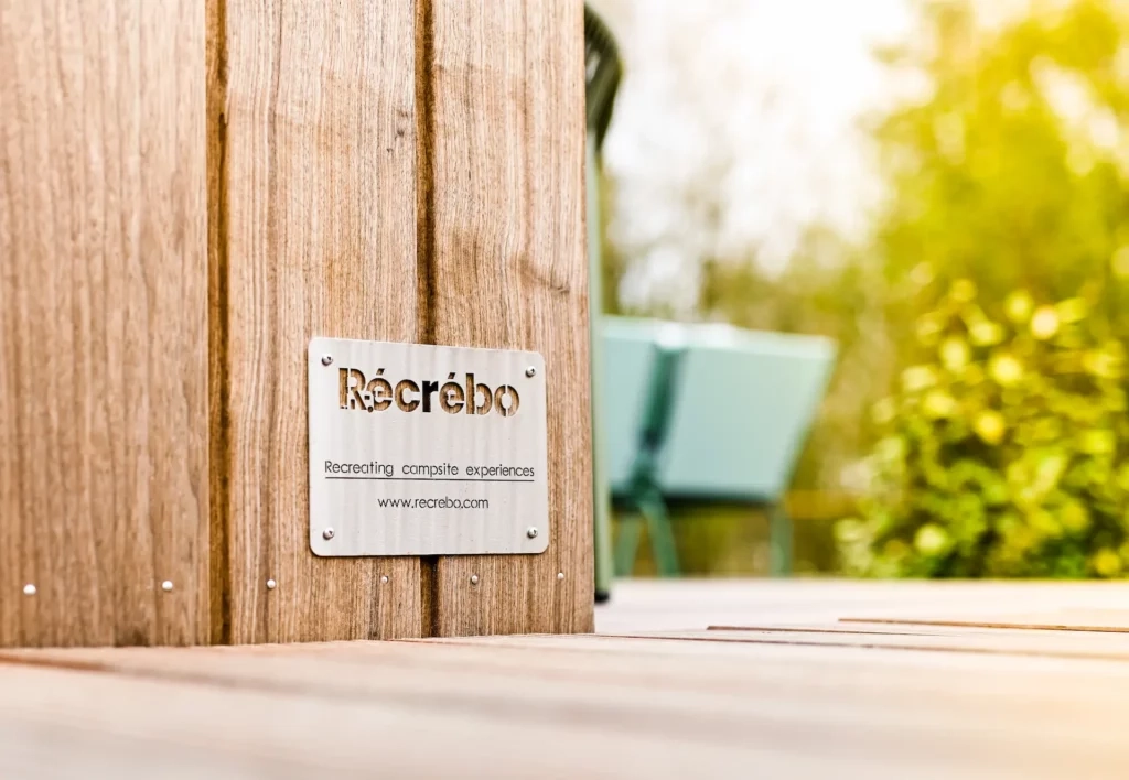 Recrebo logo op een houten wand met fel zonlicht.
